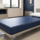 Vinyl waterproof mattress on a low-profile institutional bed in a clean healthcare facility room with folded linens and storage cabinets.